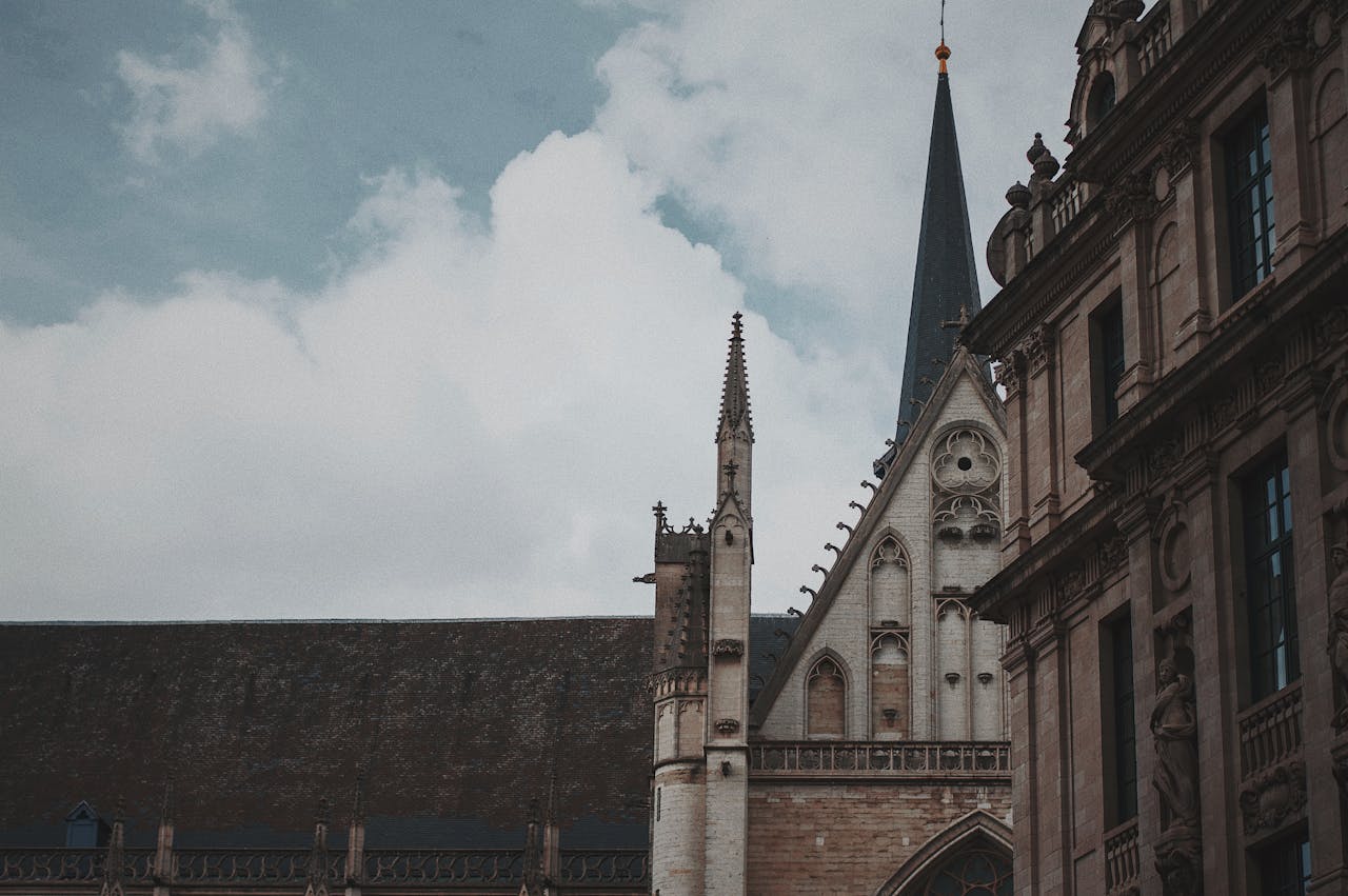 Low-angle view of a historic Gothic cathedral in Brussels showcasing intricate architectural details against a cloudy sky.